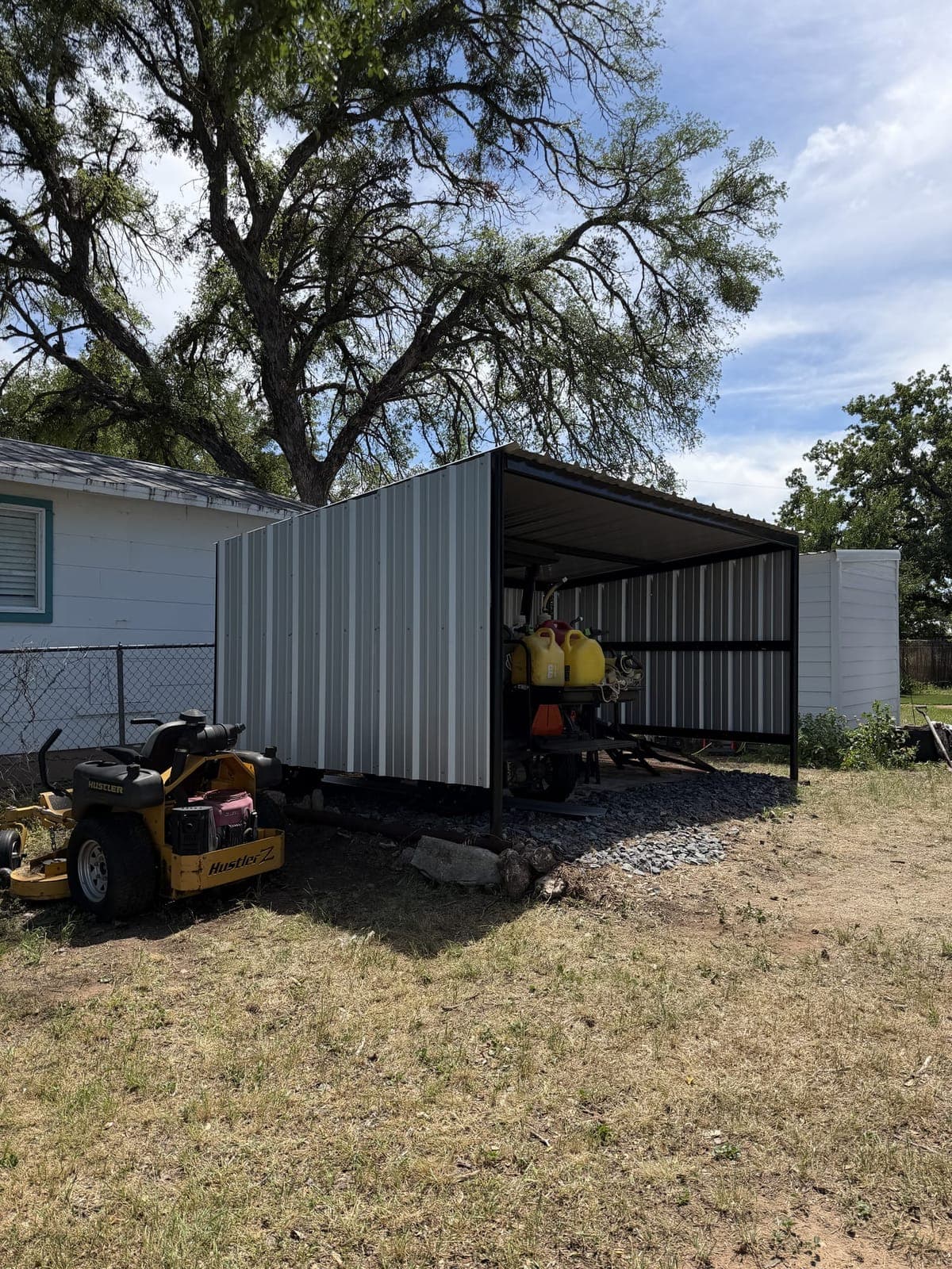 Open-front steel cover with white metal siding sheltering yard equipment
