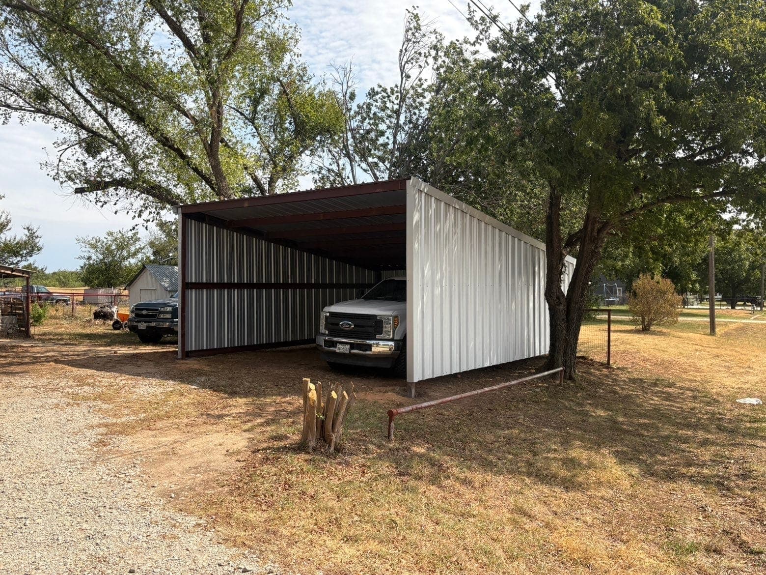 Steel carport with white metal siding on a red frame, a white Ford pickup parked underneath