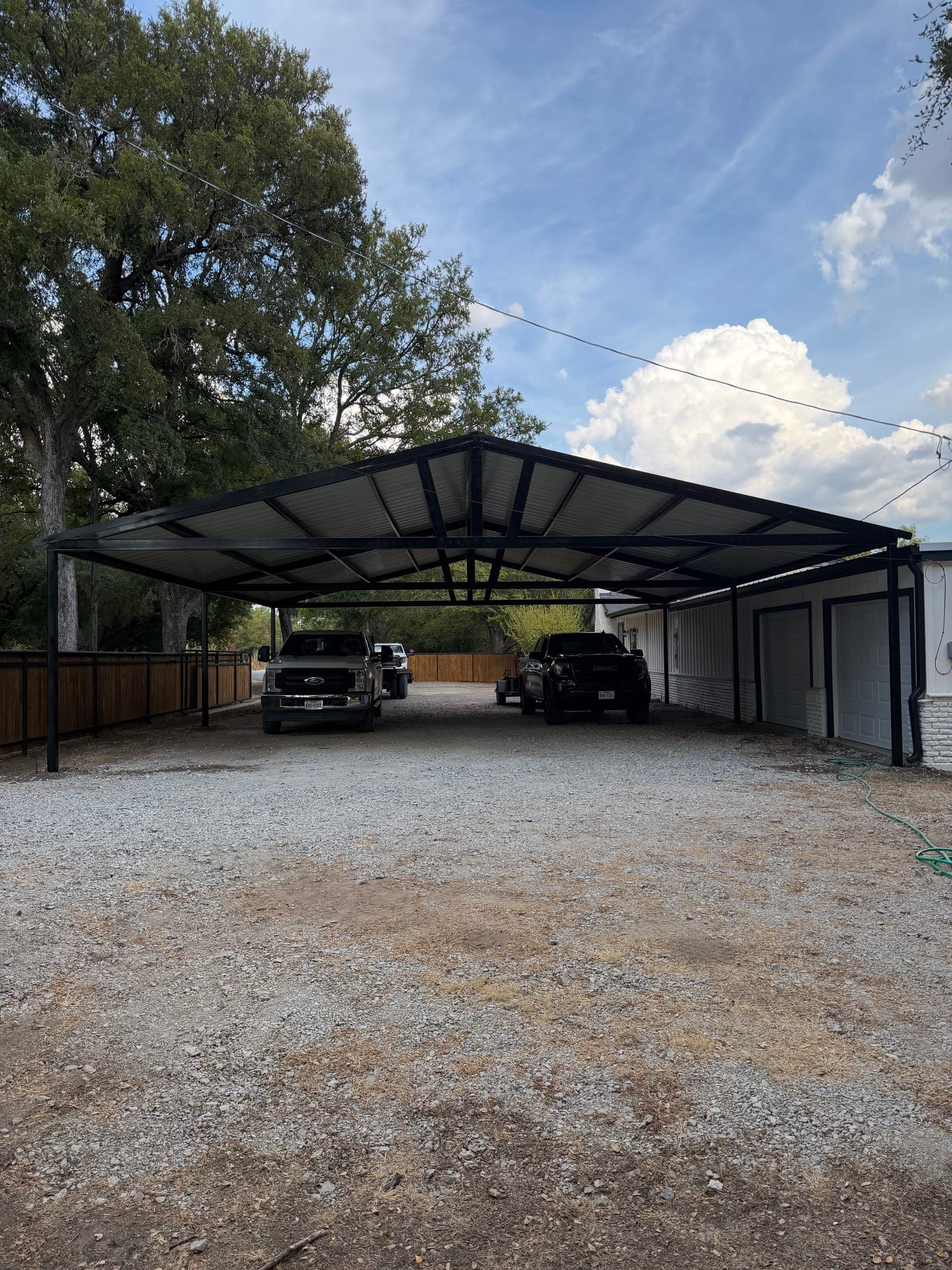 After: the same drive under a long black steel carport, trucks parked beneath it